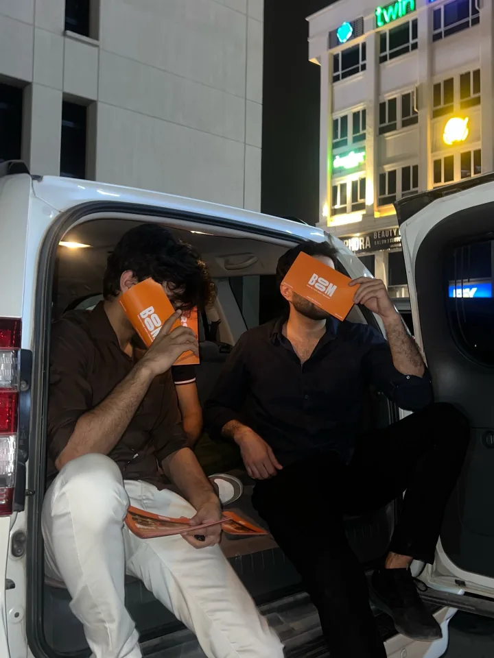 Two friends with orange BOOM boxes beside a car